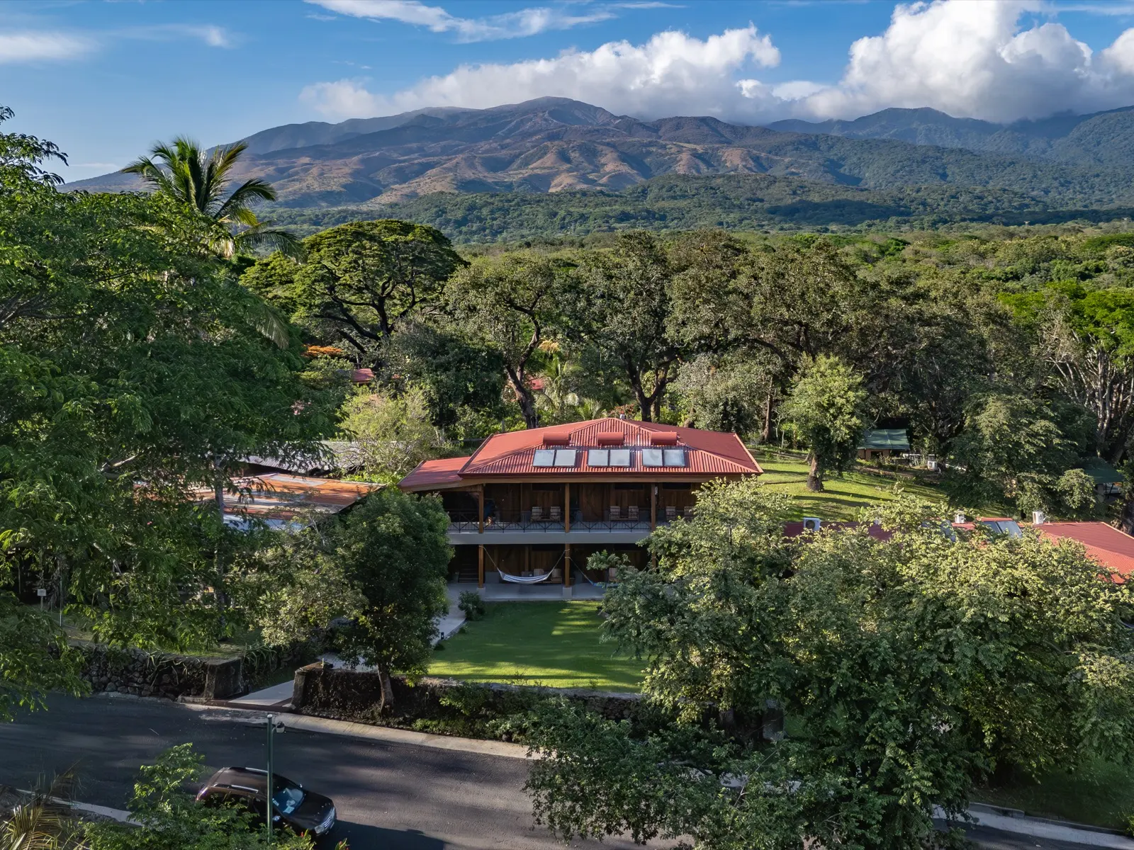Aerial view of Hacienda Guachipelín's red-roofed lodge among trees below the Rincón de la Vieja volcano range